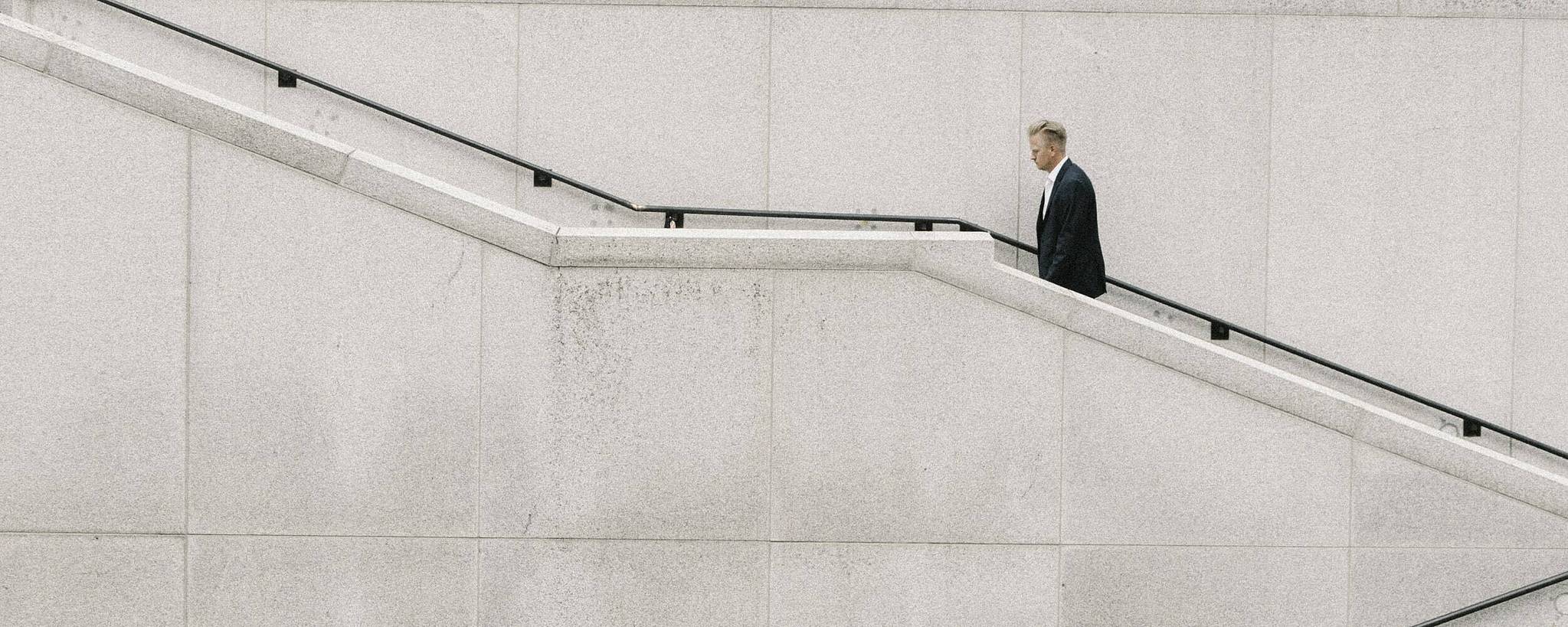 Mann im Anzug läuft graue Treppe eines Gebäudes hinauf